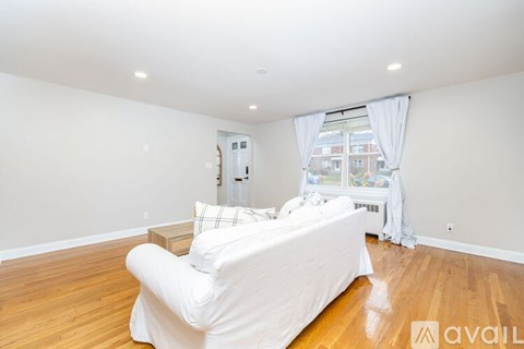 A white couch is in a large, empty room with wooden floors and a window with white curtains.
