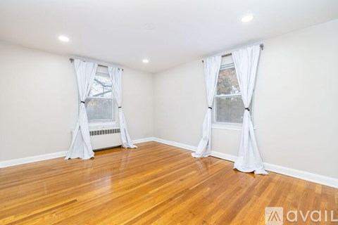 A room with wooden floors and two windows with white curtains.