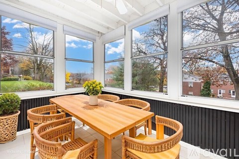 A wooden table with chairs is in front of a window with a view of trees and houses.