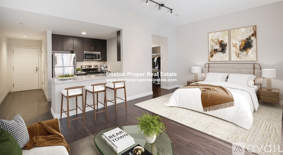 A modern bedroom with a large bed and a kitchenette area in the background.