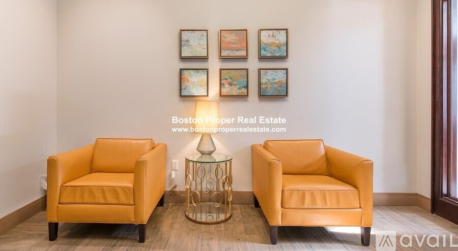 Two orange chairs are placed in front of a wall with pictures and a lamp.