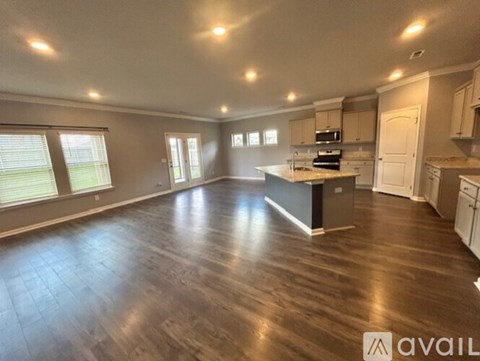 A spacious kitchen and living room with wood flooring and white walls.