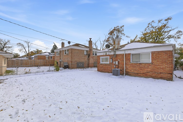 A snow-covered yard with a house and a fence in the background.