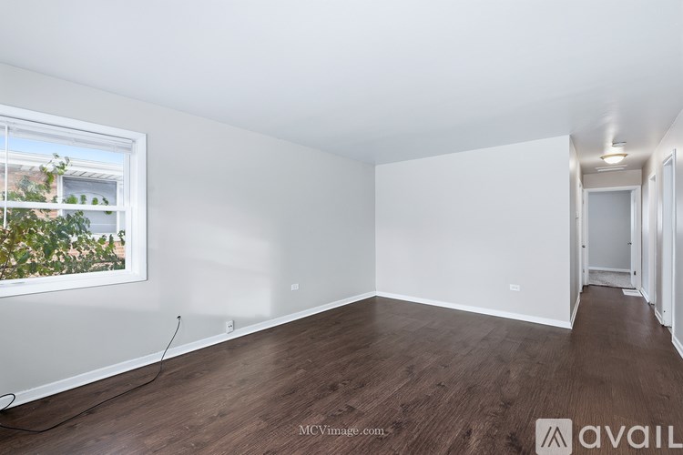 A room with wooden floors and white walls, with a window showing greenery outside.