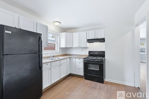 A black fridge stands in a kitchen with white cabinets and a black stove.