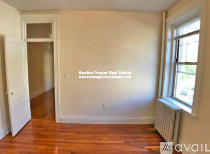 A room with wooden floors and a window with a view of trees and a building outside.