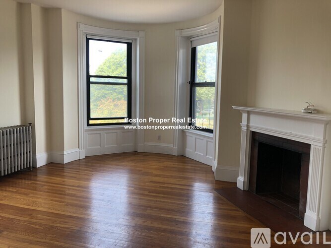 A large, empty room with wood flooring and a fireplace.
