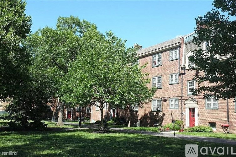 A large tree in front of a building with a red door.