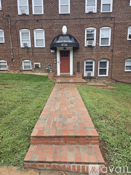 A brick pathway leads to a black and white apartment building entrance.