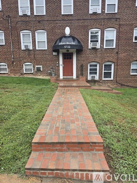 A brick pathway leads to a black and white apartment building entrance.