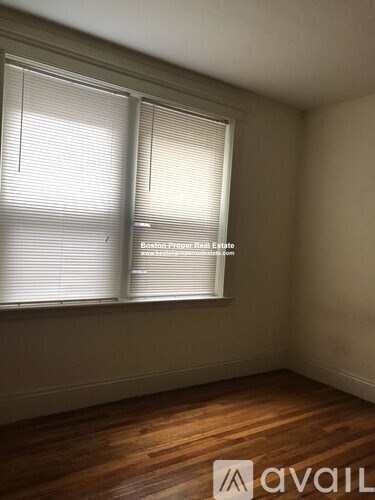 A room with wooden floors and two windows covered with blinds.