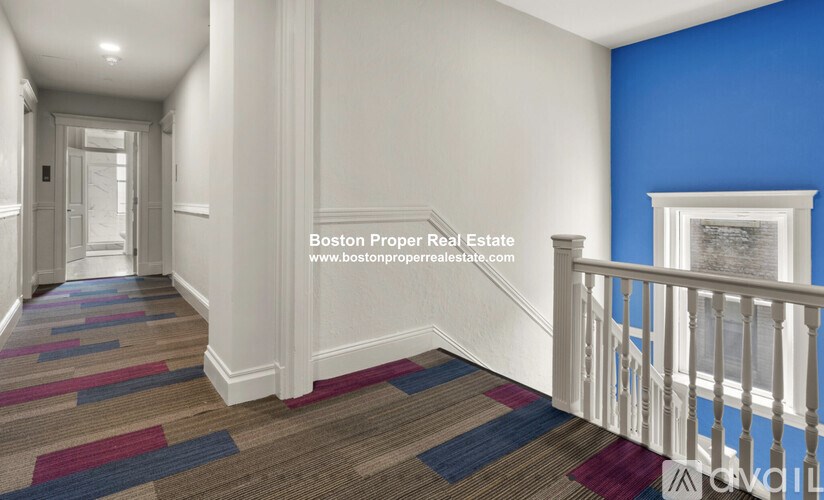 A hallway with a carpeted floor and a white railing.