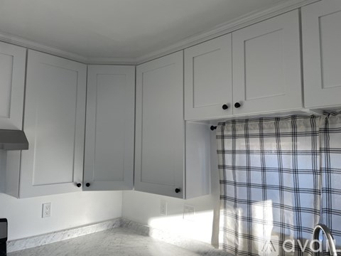 A kitchen with white cabinets and a checkered curtain.
