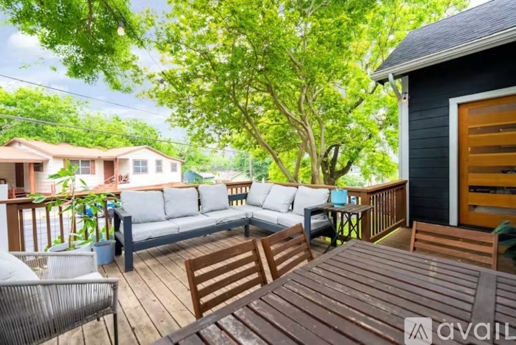 A wooden deck with a sofa and chairs is surrounded by green trees.
