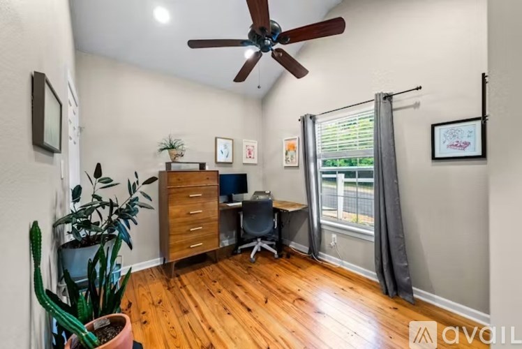 A room with a ceiling fan, a cactus, a desk with a chair, and pictures on the wall.