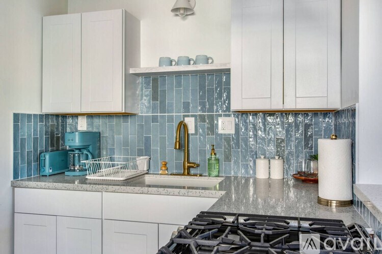 A kitchen with white cabinets and a blue kettle on the counter.