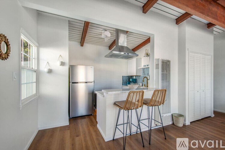 A kitchen with a white refrigerator, wooden bar stools, and a white island.