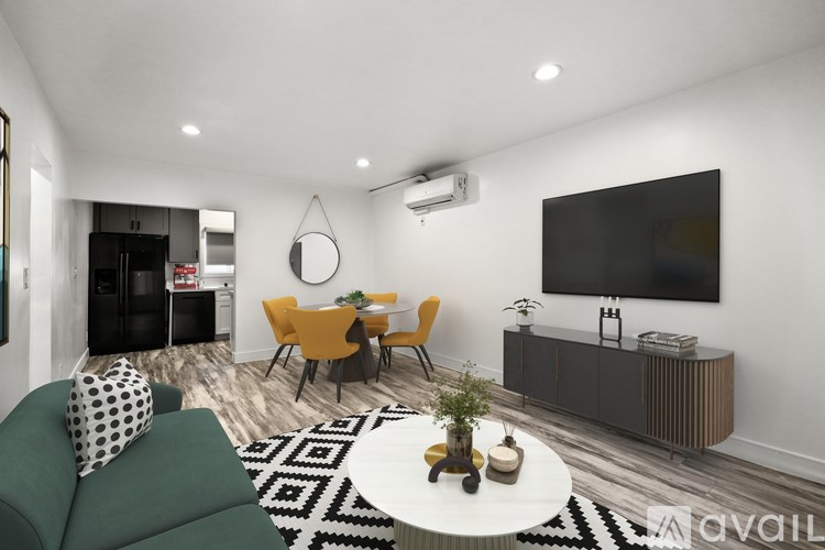 A living room with a green sofa, a yellow chair, a black and white rug, and a flat screen TV mounted on the wall.