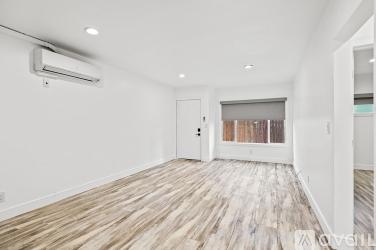 A spacious room with wooden flooring and a white wall.