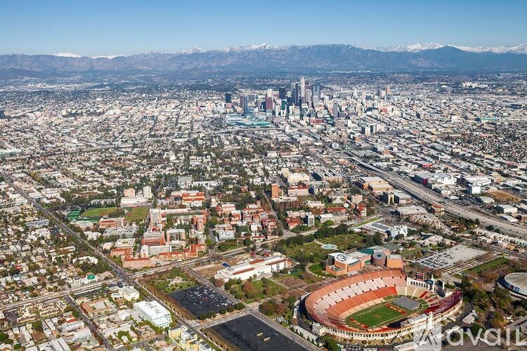 A cityscape with a large stadium in the foreground and mountains in the background.
