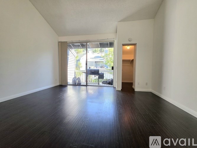 A room with wooden floors and white walls, with a sliding glass door leading to a balcony.