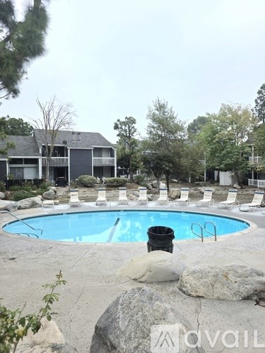 A pool surrounded by rocks and chairs with a building in the background.