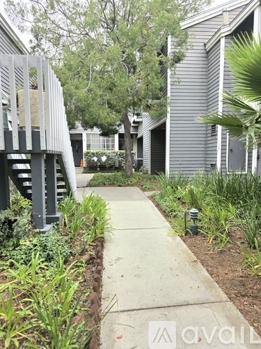 A concrete walkway leads to a house with a metal staircase on the left.