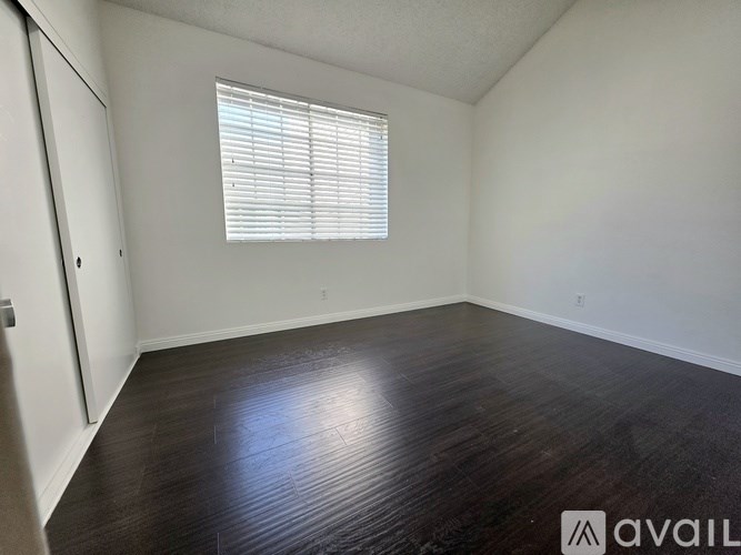 A room with wooden flooring and a window with blinds.