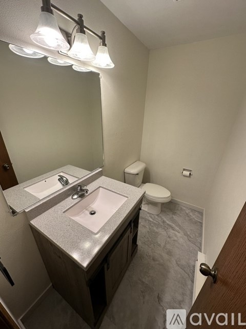 A bathroom with a sink, mirror, toilet and a light fixture.