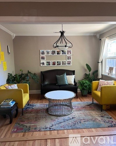 A living room with a black couch, yellow chairs, a white coffee table, and a wall with pictures and plants.