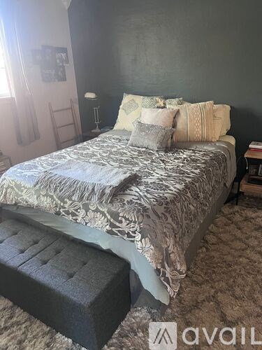 A bed with a grey and white comforter and a grey ottoman in front of it.