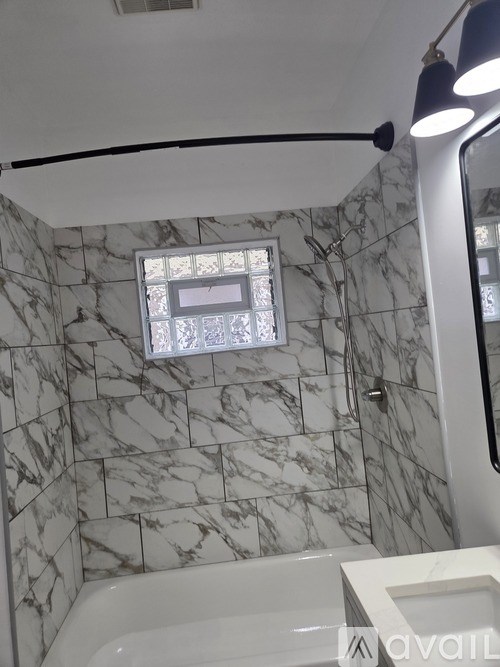A bathroom with a marble tile wall and a white tub.