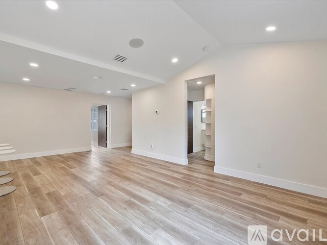 A spacious room with wooden flooring and white walls.