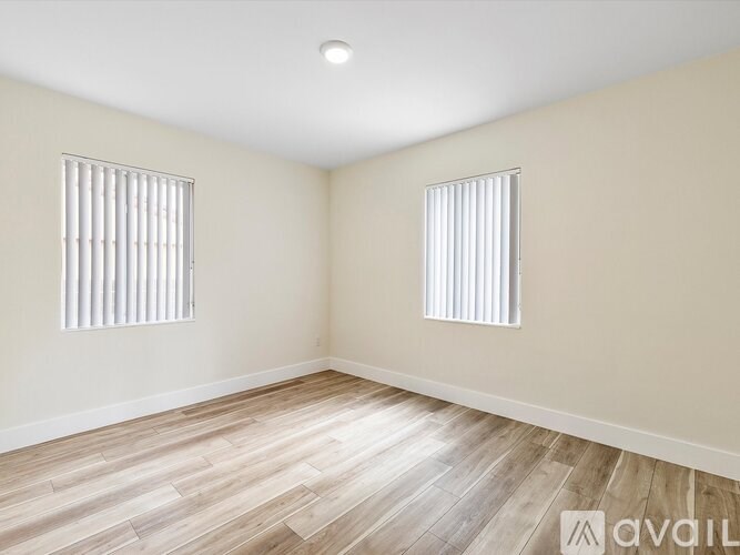 A room with wooden flooring and two windows with blinds.