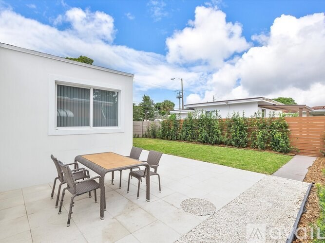 A patio with a table and chairs is set up outside a white house.
