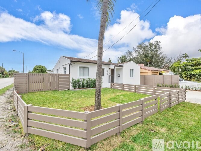 A house with a wooden fence and a palm tree in front.