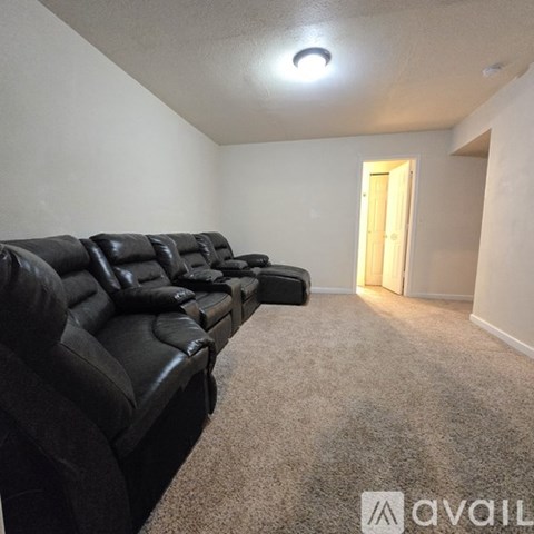 A black leather couch in a room with a carpeted floor and a door in the background.