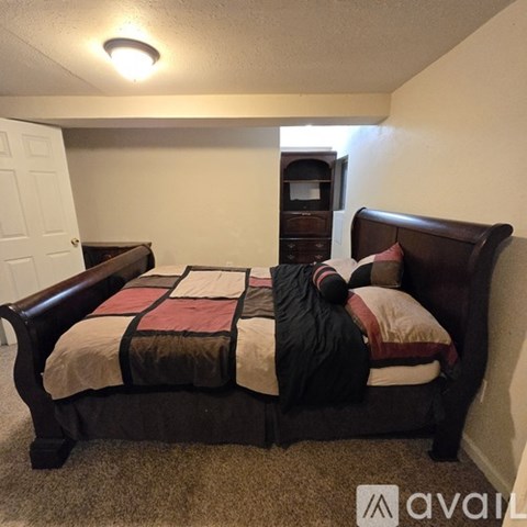 A bed with a black frame and a striped comforter is in a room with a carpeted floor.