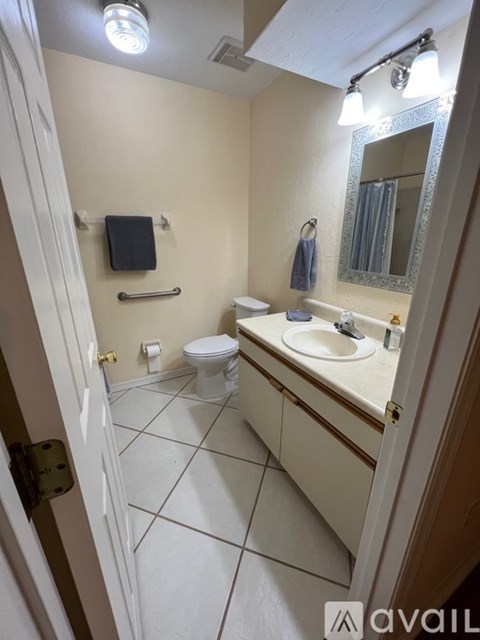 A bathroom with a toilet, sink, mirror, and light fixture.