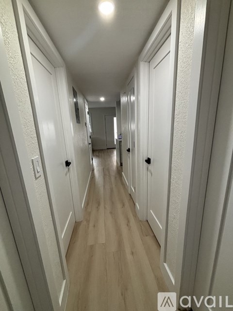 A long hallway with white doors and wood flooring.