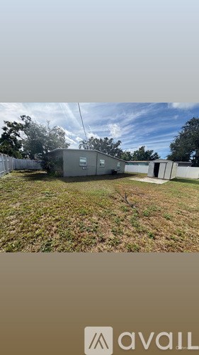 A large grey building is situated in a grassy area with trees in the background.
