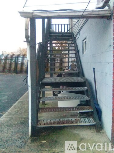 A metal staircase with a white wall on one side and a black fence on the other.