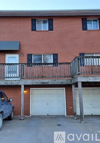 A red brick building with a balcony and a car parked in front.