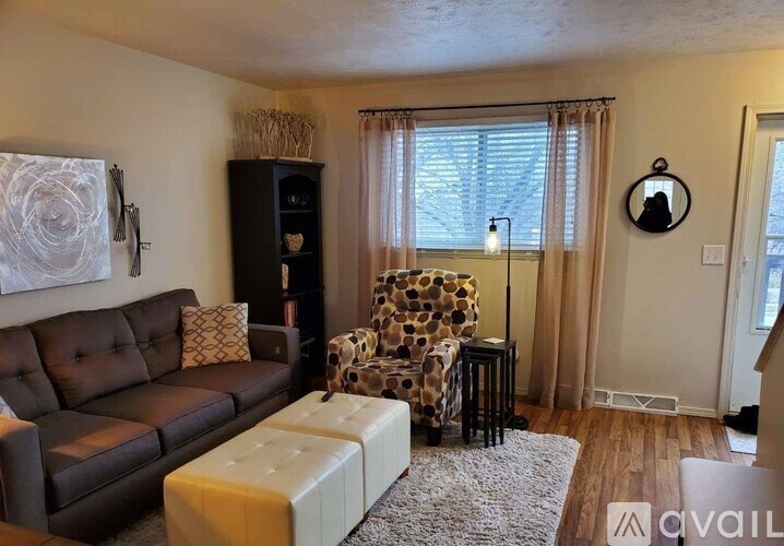 A living room with a brown couch, a leopard print chair, and a white ottoman.
