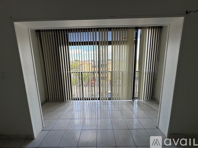 A room with a view of a parking lot through a window with blinds.