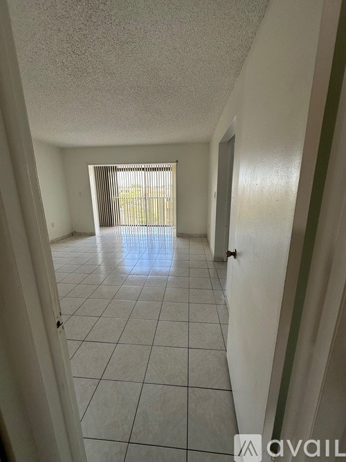 A hallway with white tile flooring and a window with blinds.