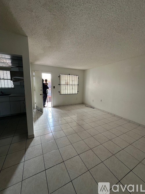 A person stands in a room with a tiled floor and a window with bars.