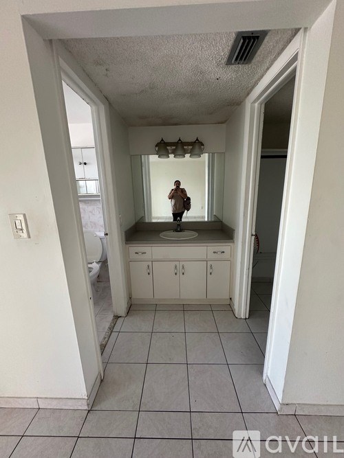 A person is standing in a white hallway with a cabinet and a mirror.