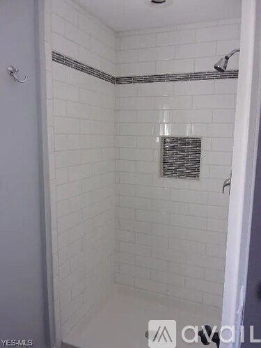 A white tiled shower with a silver shower head.