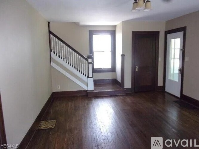 A room with wooden floors and a staircase leading to another room.